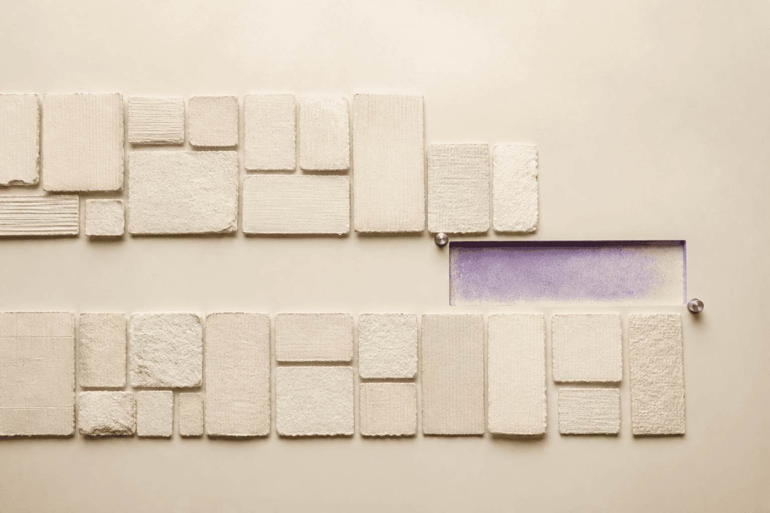 Generated top-down illustration of two rows of ivory paper-and-plaster tiles interrupted by an empty violet rectangular imprint marked by two small metal registration pins.