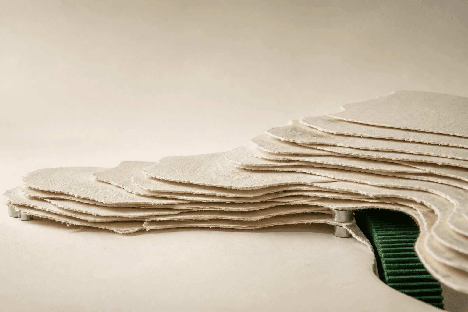 Generated editorial illustration of a low landscape made from irregular layers of ivory paper, held above a few metal spacers, with a forest-green ribbed strip descending into a dark fissure.